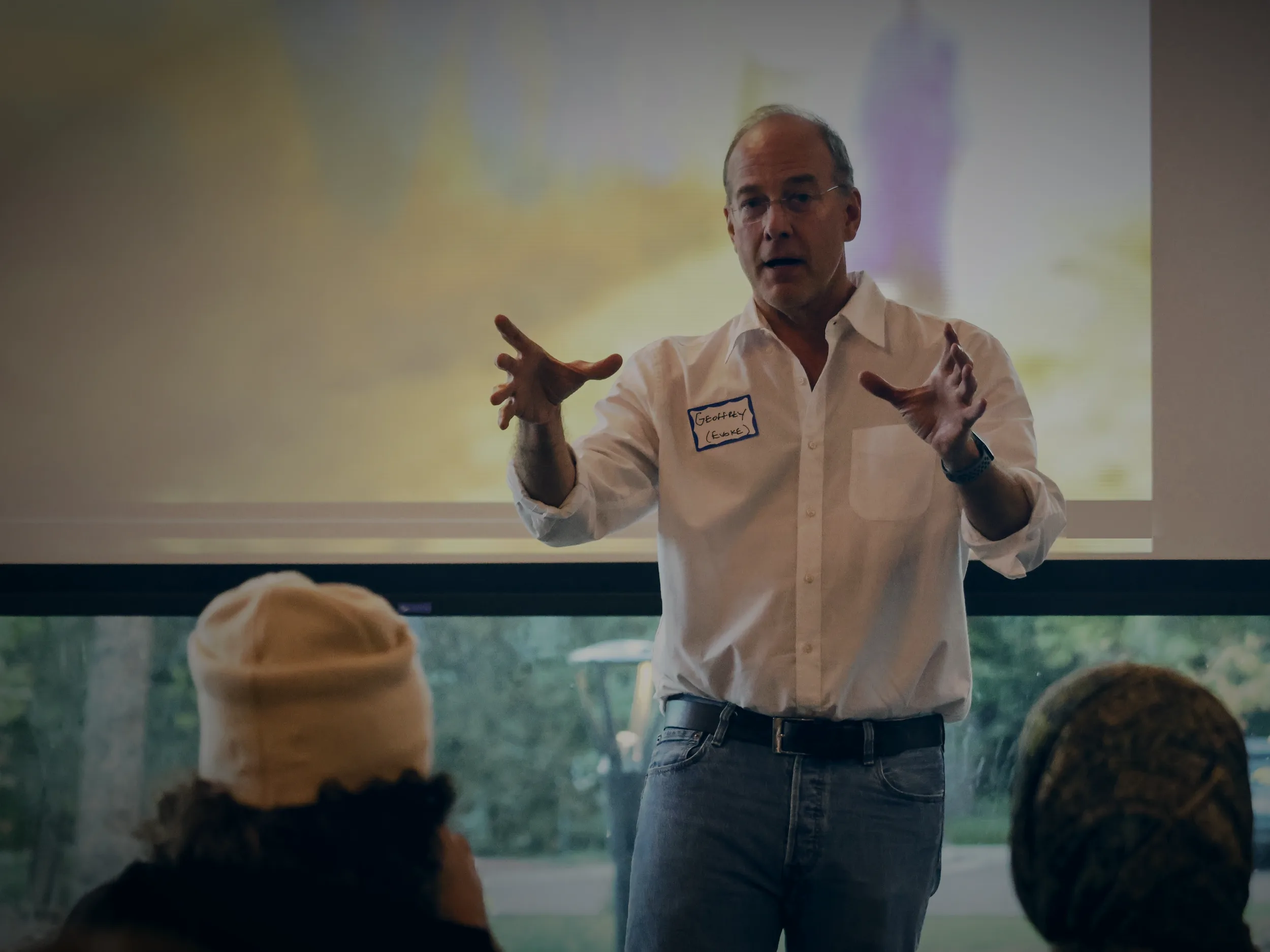 Geoffrey Kirkman hablando ante un grupo de jóvenes en un sprint de diseño de EVOKE en Boulder, con una imagen proyectada en la pantalla detrás